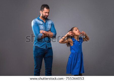 A young black man standing with folded arms while his young teenage daughter acting silly
