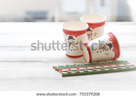 Festive still life with three glasses with a picture of a snowman on a white wooden table, multicolored sticks, a country background on a sunny day
