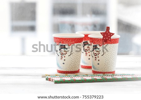 Festive still life with three glasses with a picture of a snowman on a white wooden table, multicolored sticks, a country background on a sunny day