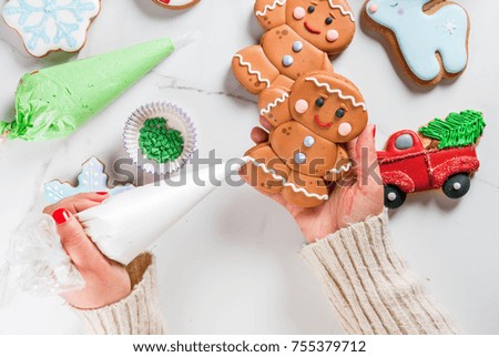 Preparation for Christmas, the girl (hands in the picture) decorates homemade hand-made traditional gingerbread with multicolored sugar icing, biscuits, white marble table. top view copy space