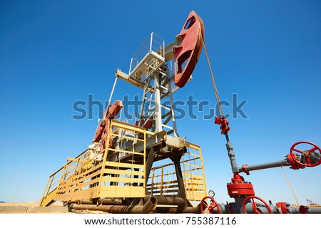   Oil pump are working in the blue sky background.
A oil pump is the overground drive for a reciprocating piston pump in an oil well. World Oil Industry. Atyrau region. Kazakhstan.