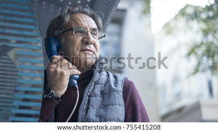  Senior man talking on public payphone in outdoors Royalty-Free Stock Photo #755415208