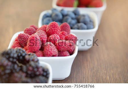 Berries: raspberries, blueberries, blackberries, strawberries. Fresh summer berries in a white bowl on a wooden background.