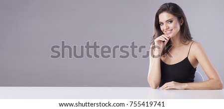 Elegant woman in black dress sitting behind the table and showing something/