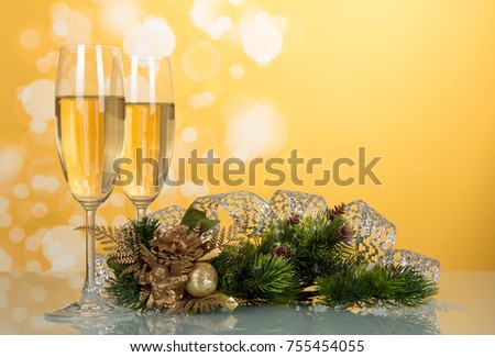 Two glasses with champagne, pine branch decorated with ribbon, New Year's souvenir on bright yellow background