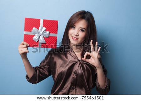 Young Asian woman show OK with a gift box on blue background