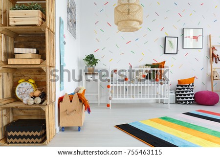 Colorful carpet in bright baby's room with wooden furniture and plant on white cabinet