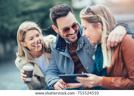 Group of smiling friends using digital tablet outdoors