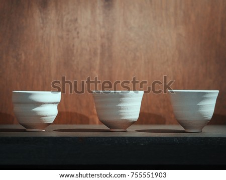 Raw clay ceramic bowls on wood table over brown wooden background.
