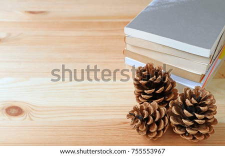Natural pine cones with stack of books on light brown wooden table, some free space for text and design