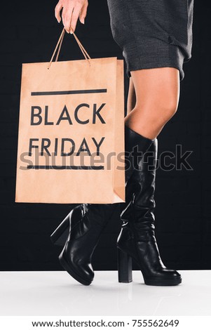 cropped view of woman holding shopping bag with black friday sign, isolated on black