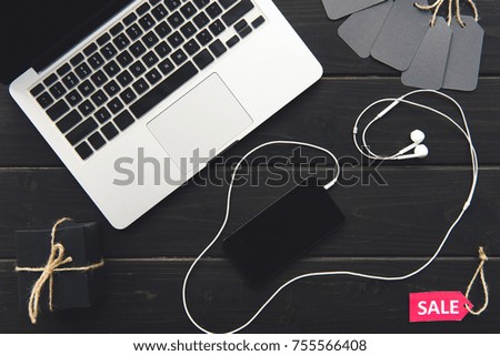 top view of laptop, sale tags, gift box, smartphone with earphones on wooden table  