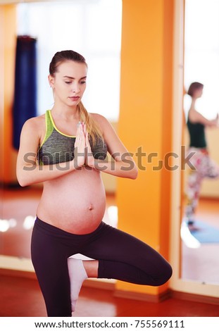 Beautiful pregnant woman performs aerobic exercises or asanas with a group of yoga in the fitness center