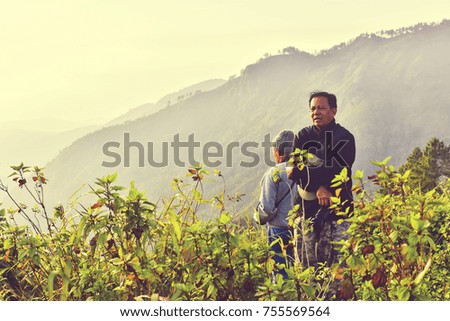 Photographer in Winter Clothes With Camera on Tripod.Happy Standing in Green Grass Meadow on Top of Mountain Peak Edge Cliff Enjoying Nature Sunset or Sunrise.Beautiful Freedom  World Concept.