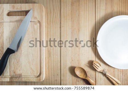 Top view of prepare cooking : knife on chopping board. and spoon, fork and white dish on wooden table.