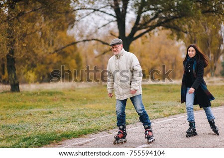 The old man goes on rollers with his daughter in the autumn park. Happy pension. Active old people.The old man goes on rollers with his daughter in the autumn park. Happy pension. Active old people.