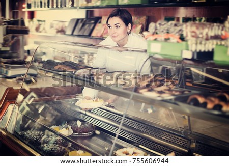 Glad female assistant helping to choose dessert in confectionery