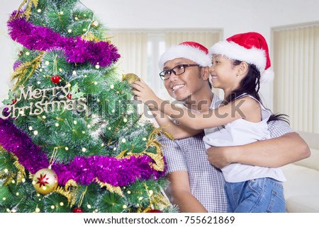 Picture of a little girl and her father decorating a Christmas tree with a ball ornament at home