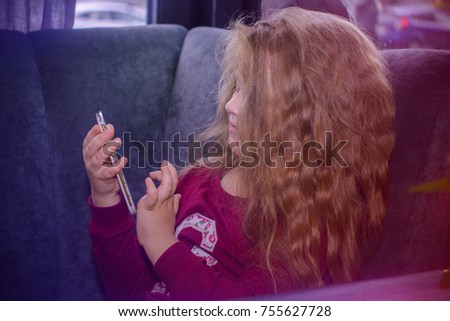 Young blonde girl with mobile telephone sitting in cafe. About kids and technologys