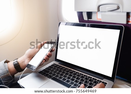 Close up of young man sitting at airplane and using laptop with blank screen and open laptop, back view