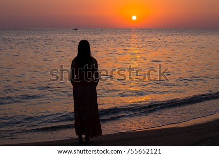 Girl with dark hair stand on the seashore and meets the sunrise. Dawn over the sea. Concept of beach rest and relaxation