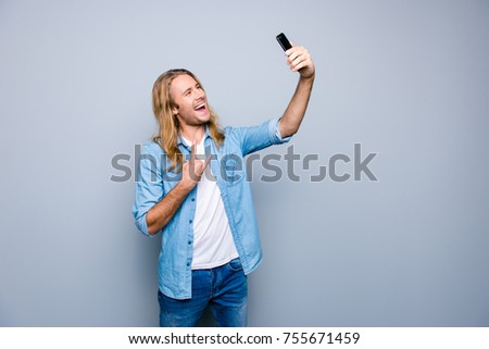 Portrait of crazy student making selfie and gesturing rock and roll symbol standing over grey background