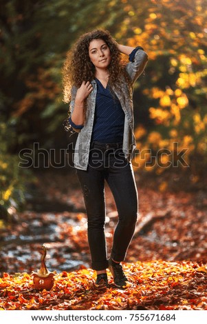  Young curly woman walking in the forest at autumn, sunrise in the background                              