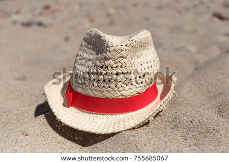 Wicker hat with red band laying on the sea sand.