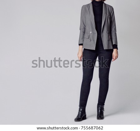 Woman wearing smart outfit with black turtleneck, grey elegant blazer, skinny jeans and ankle boots isolated on gray background. Copy space       
