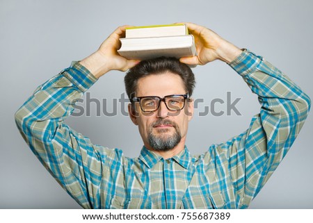 teacher man holding books on his head, wearing glasses, isolated in studio on gray background