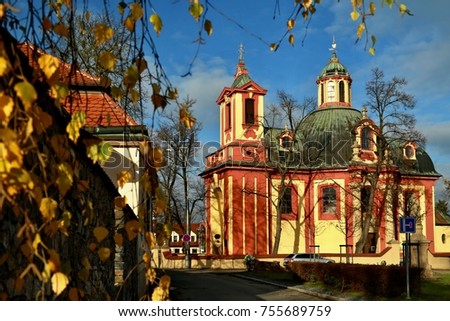 Red and yellow Church of Saint Jacob the Bigger in Kunratice close to Prague, picture taken in November sun with blue sky and birch leaves 