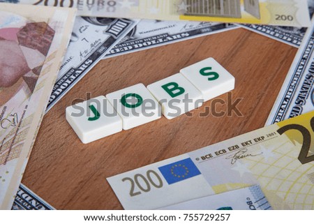 Jobs word with green letters among cash dollar, euro and turkish lira banknotes on wooden background.