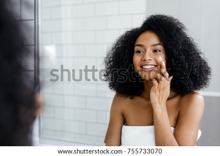 Happy young woman applying face cream with finger in bathroom Royalty-Free Stock Photo #755733070