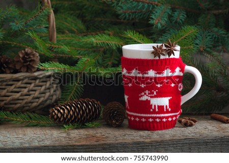 Christmas handmade knitted mug with tea, red ligntning lantern and Santa's helper hat on the rustic background