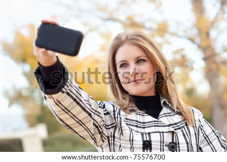 Pretty Young Woman Taking Picture with Camera Phone in the Park One Fall Day.