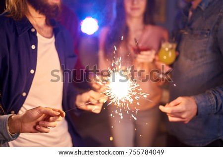  Group of friends having fun with sparklers.  young people laugh. celebrating New Year together. Group of beautiful young people in Santa hats. Blur Background 