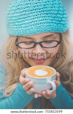 Woman holding a cup of hot art latte in the coffee shop in winter season.