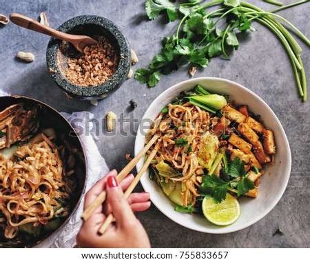 Authentic Vegetarian vegan tofu  Nok Chou padthai noodle with tamarind sauce. Hand holding chopsticks. Crush peanut in rock mortar and pan on the side. Coriandre on loft style grey cement table. Royalty-Free Stock Photo #755833657