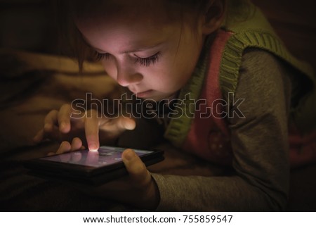 Cute little girl playing with a smartphone on the bed.