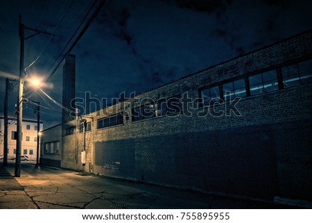 Scary dark city Chicago alley at night next to an urban factory with smokestack.
