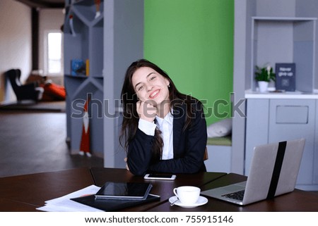 Confident attractive girl, employee of company thought with smile on face and stares into distance in front of her, leaning head against arm and continuing to work behind laptop, sitting at modern