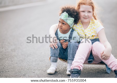 two bestfriend sitting on skateboard outdoors. Redhead little girl and african girl. The concept of friendship and intercultural communication