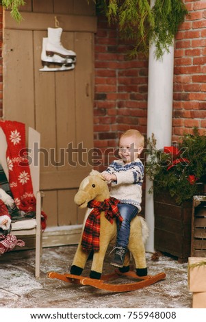 Playful smiling happy cute little child boy dressed in sweater and jeans sitting on a rocking horse in decorated New Year room at home. Christmas good mood. Lifestyle, family and holiday 2018 concept