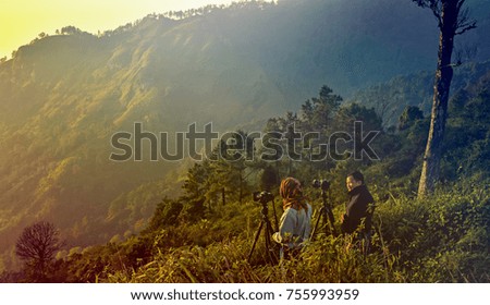Two of Mature Photographer Traveler Enjoying The Nature Taking Photo on Sunset Mountain Peak.Fiery Orange Sunrise Sky Cloud. Sunset of Gold Background.