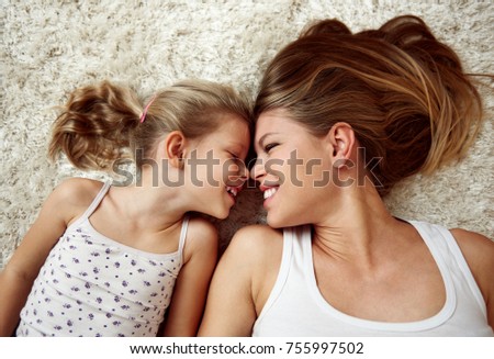 Beauty portrait of young mother with little daughter lying on carpet and smiling, looking at each other. 