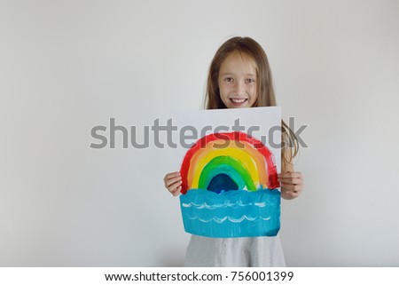 The happy girl with the children's bright drawing of a rainbow in hands on a white background