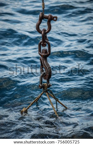 Object being raised with crane from the sea. Focus on the lifting hook connected on wires in the sea. Fairly calm sea in the background.