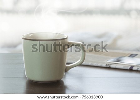A cup of coffee on teak wood table with blurred mobile phone on newspaper background. Hot coffee mug and newspaper.