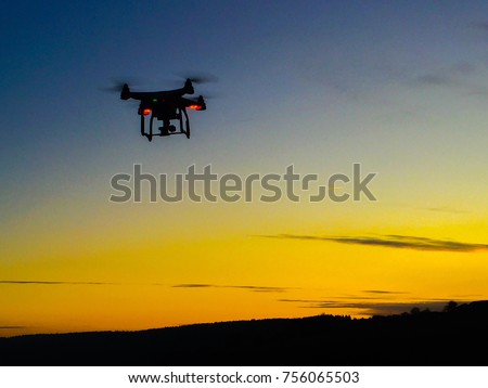 Drone with red lights on flying into a blue and orange sunset