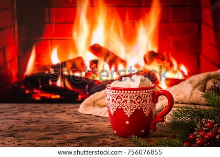 Mug of hot chocolate or coffee with marshmallows in a red mug on vintage wood table in front of Fireplace as a background. Christmas or winter warming drink.